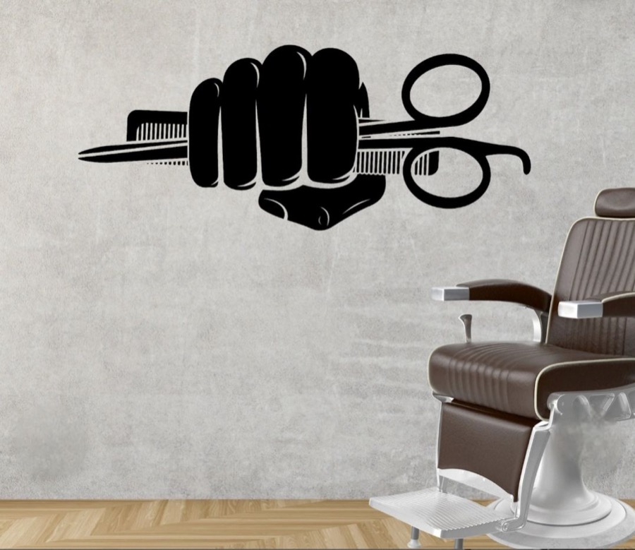 Barber chair beneath a wall decal of a fist holding scissors and a comb